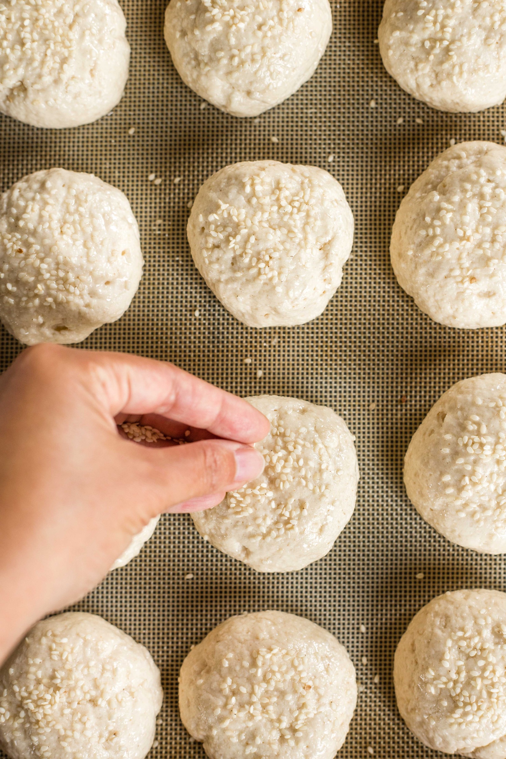 Sprinkling sesame seeds on top of gluten-free slider bun dough.