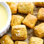 GF soft pretzel bites on parchment paper with bowl of cheese sauce