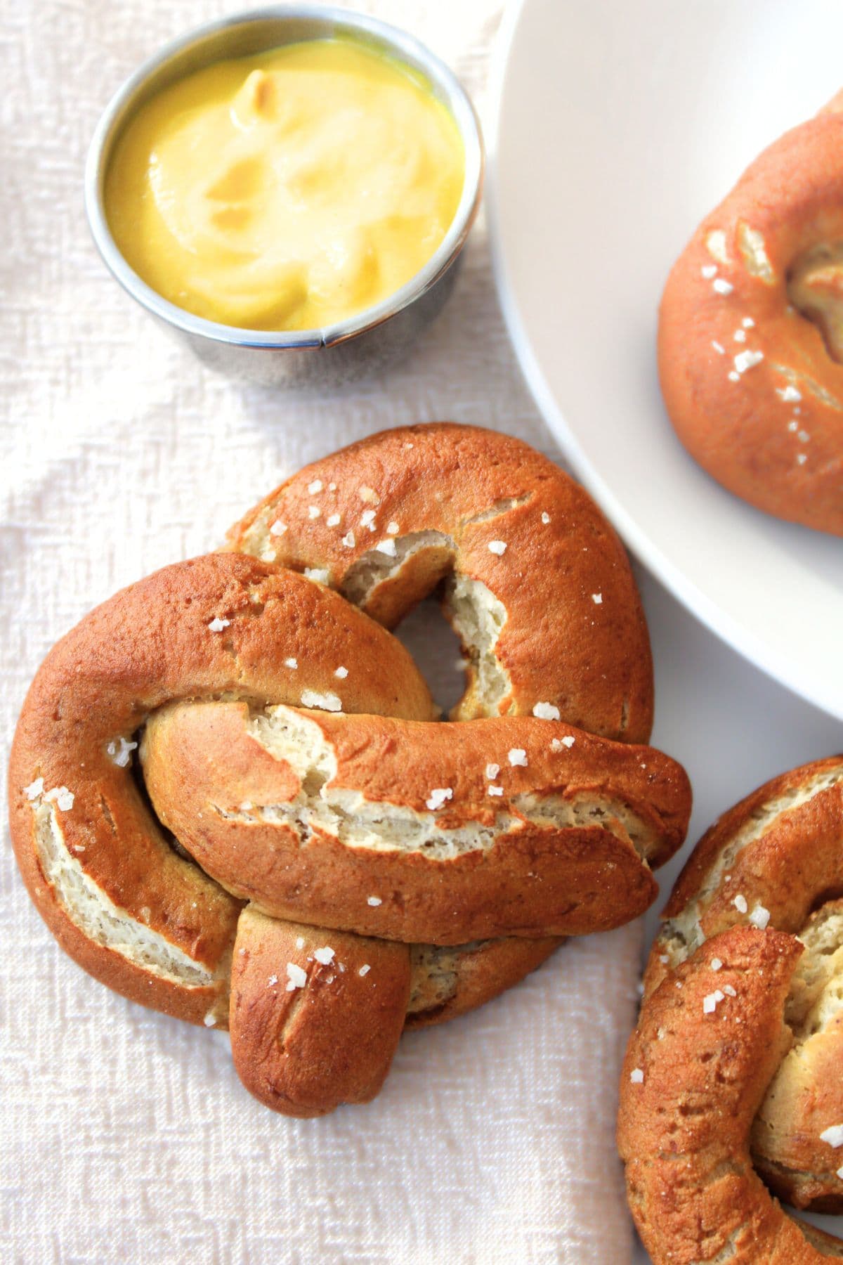 Top down view of gluten-free soft pretzels and mustard on tablecloth