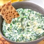 A bowl of spinach dip with a cracker