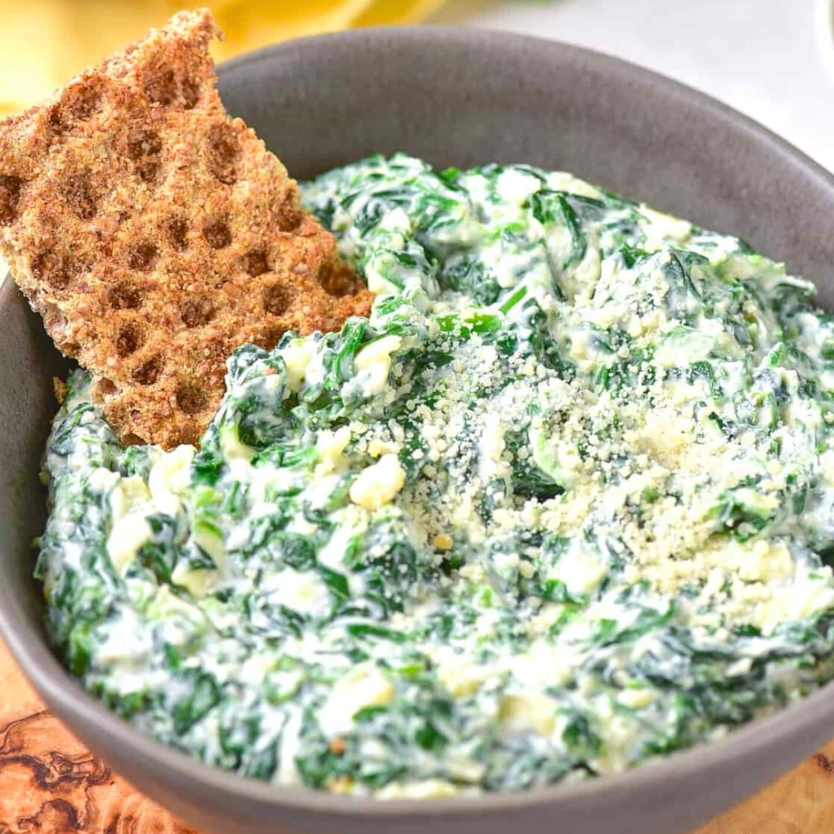 A bowl of spinach dip with a cracker