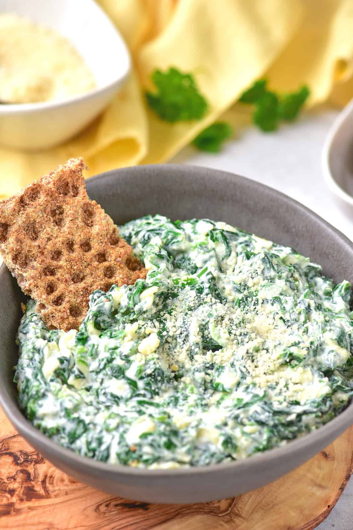 A cracker in a bowl of spinach dip.