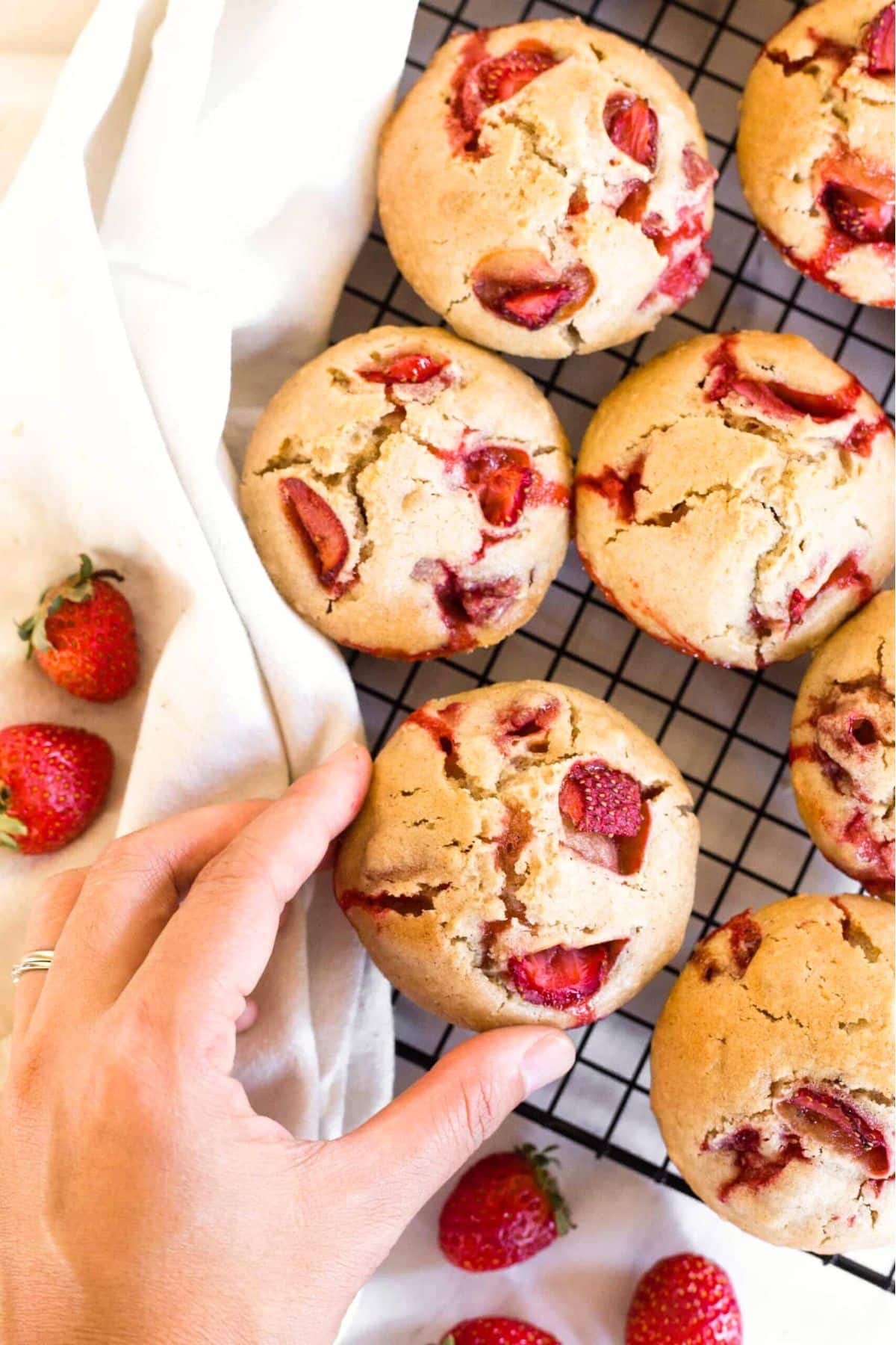 Hand reaching for a gf strawberry muffin from a cooling rack