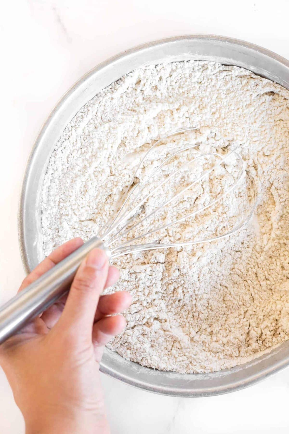 Hand whisking flour mixing in metal bowl.