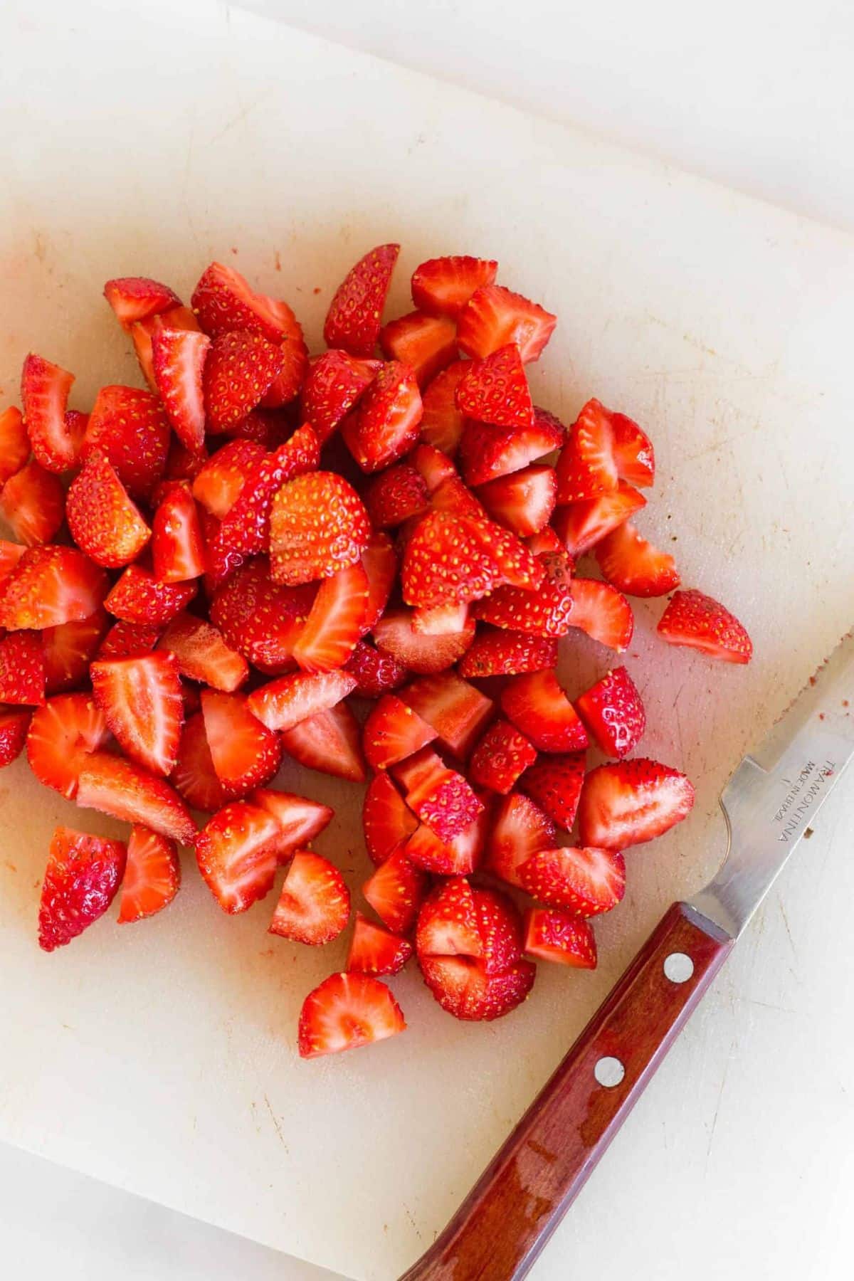 Cut strawberries on chopping board with knife.