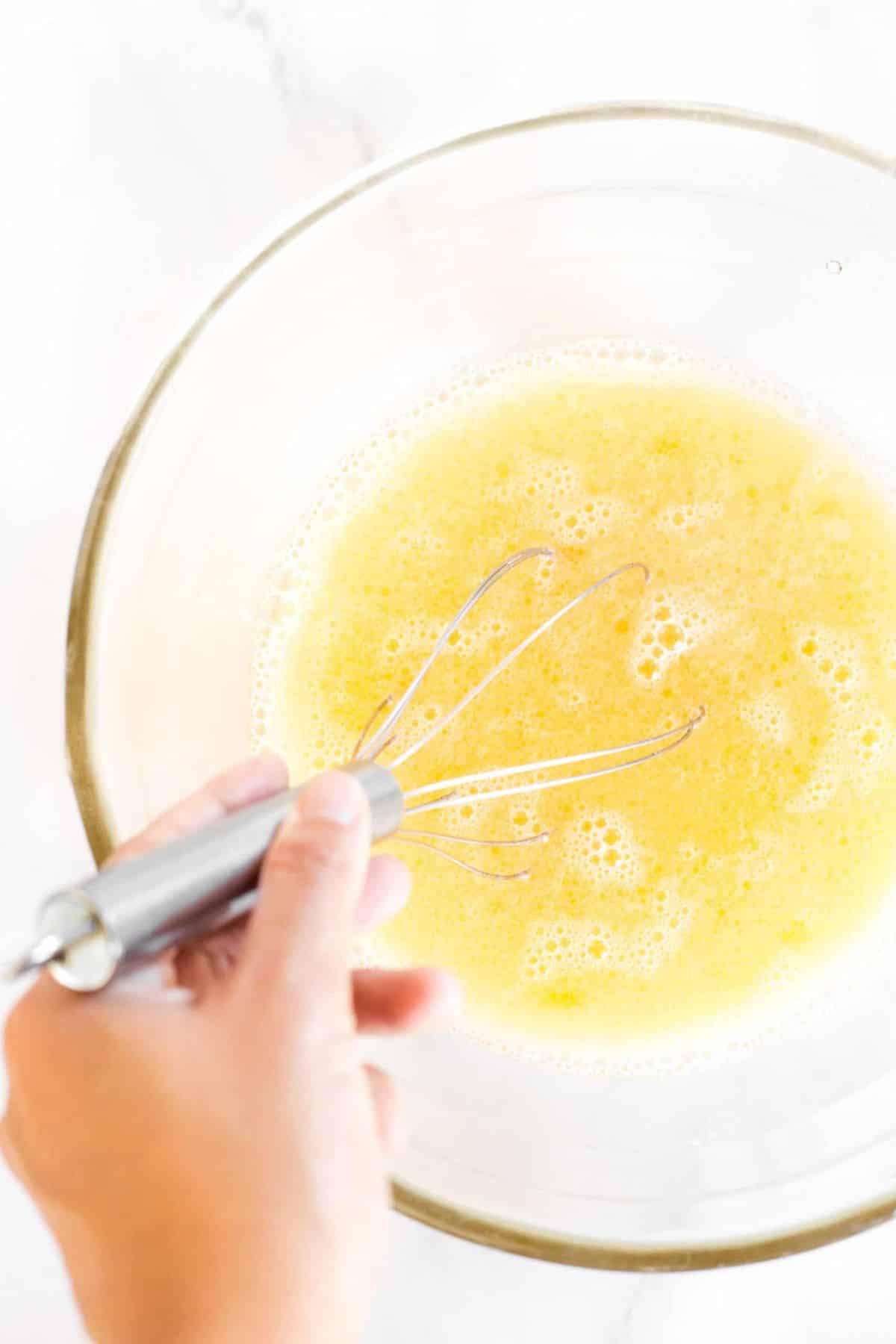 Whisking pale yellow liquid mixture in glass bowl.
