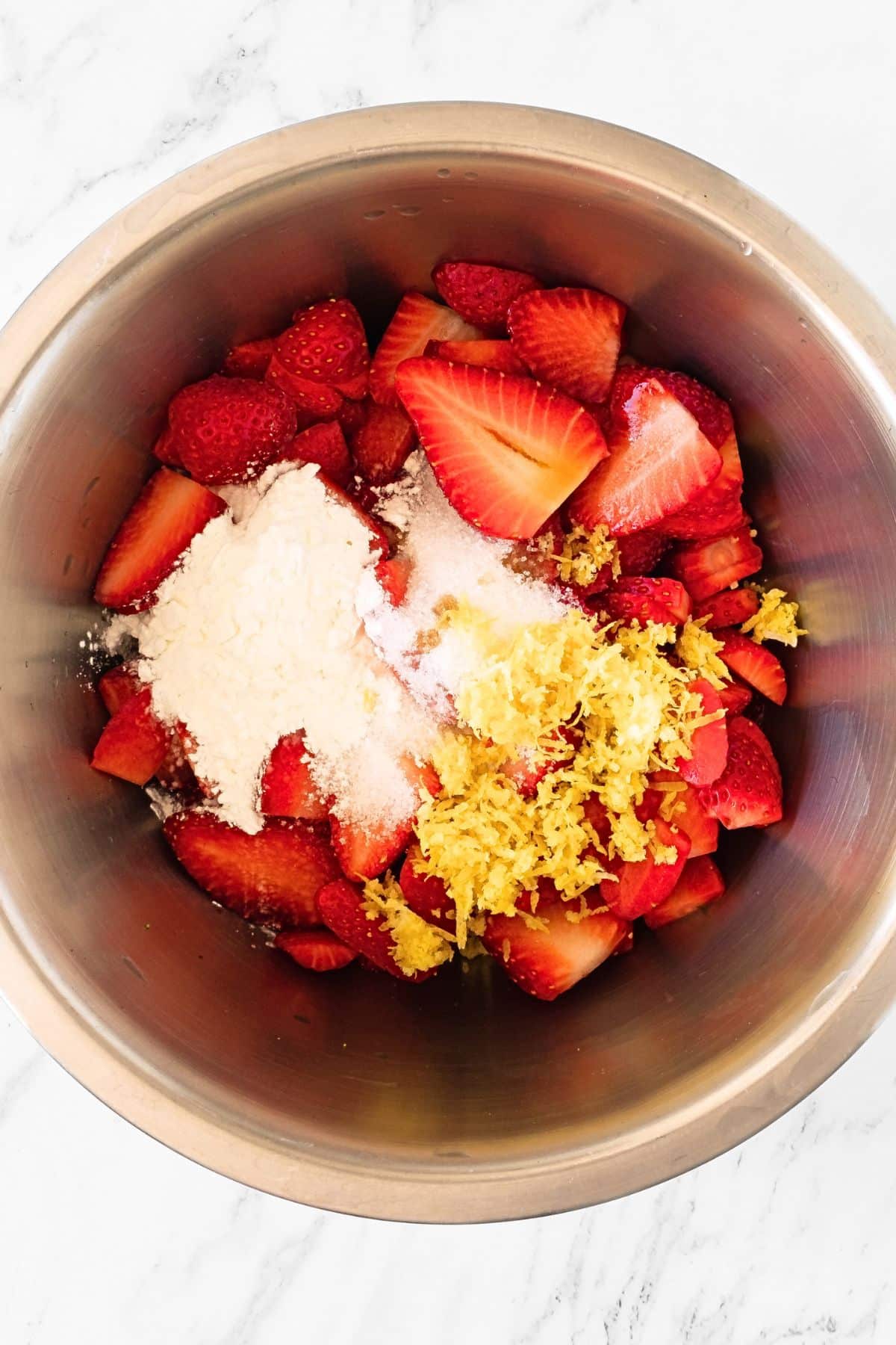 Mixing fresh strawberries, sugar, lemon zest, and corn starch in metal bowl.