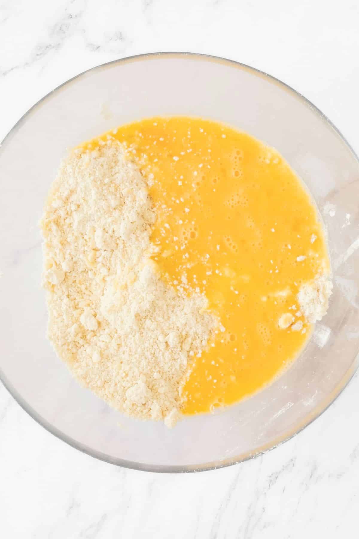 Beaten egg poured on top of flour mixture in glass bowl.