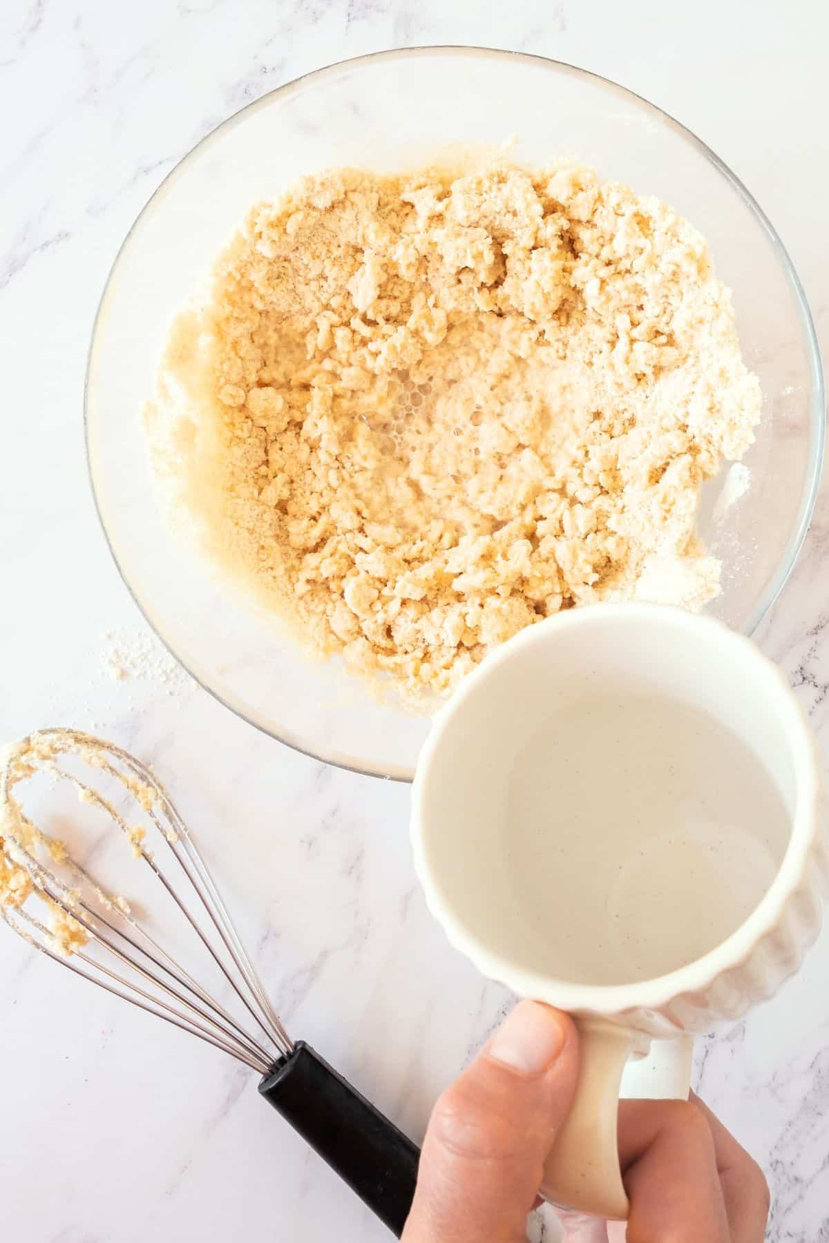 Pouring ice water into pie dough mixture.