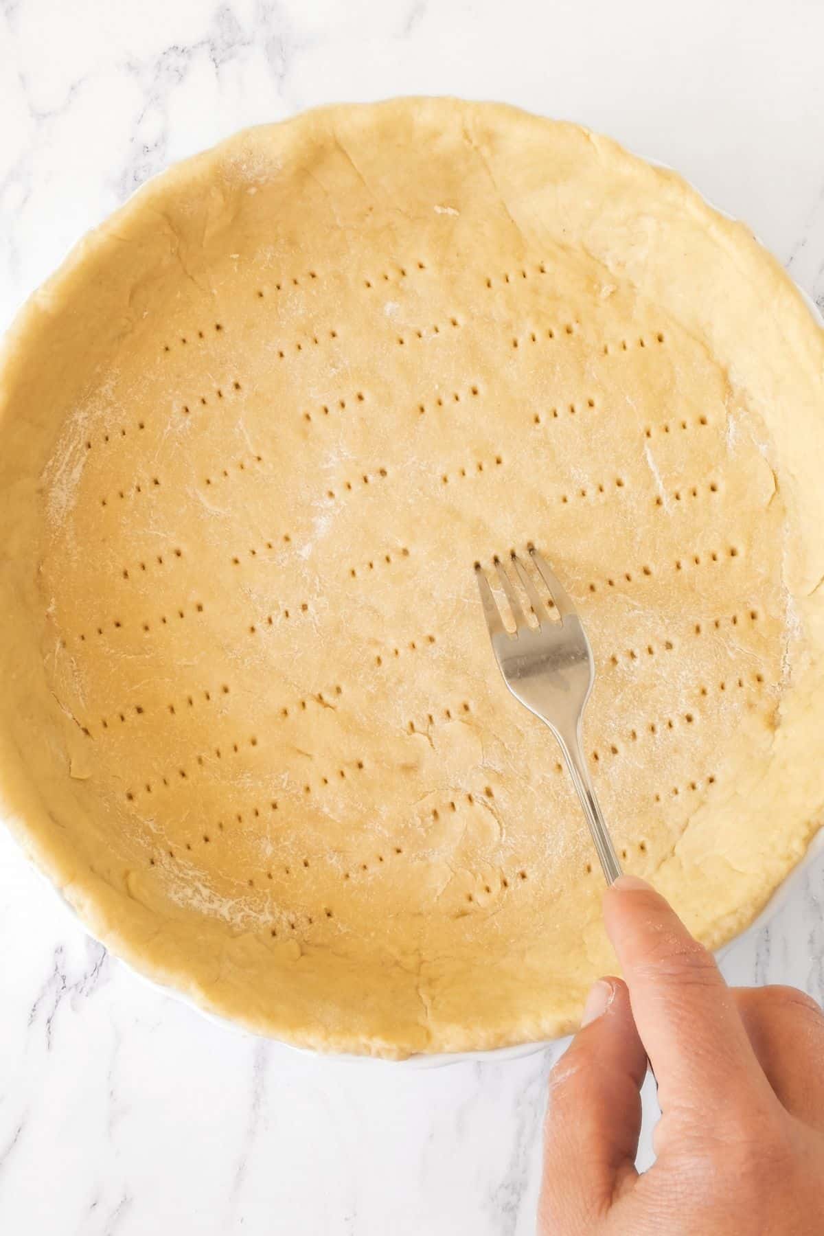 Using a fork to poke holes into pie dough.