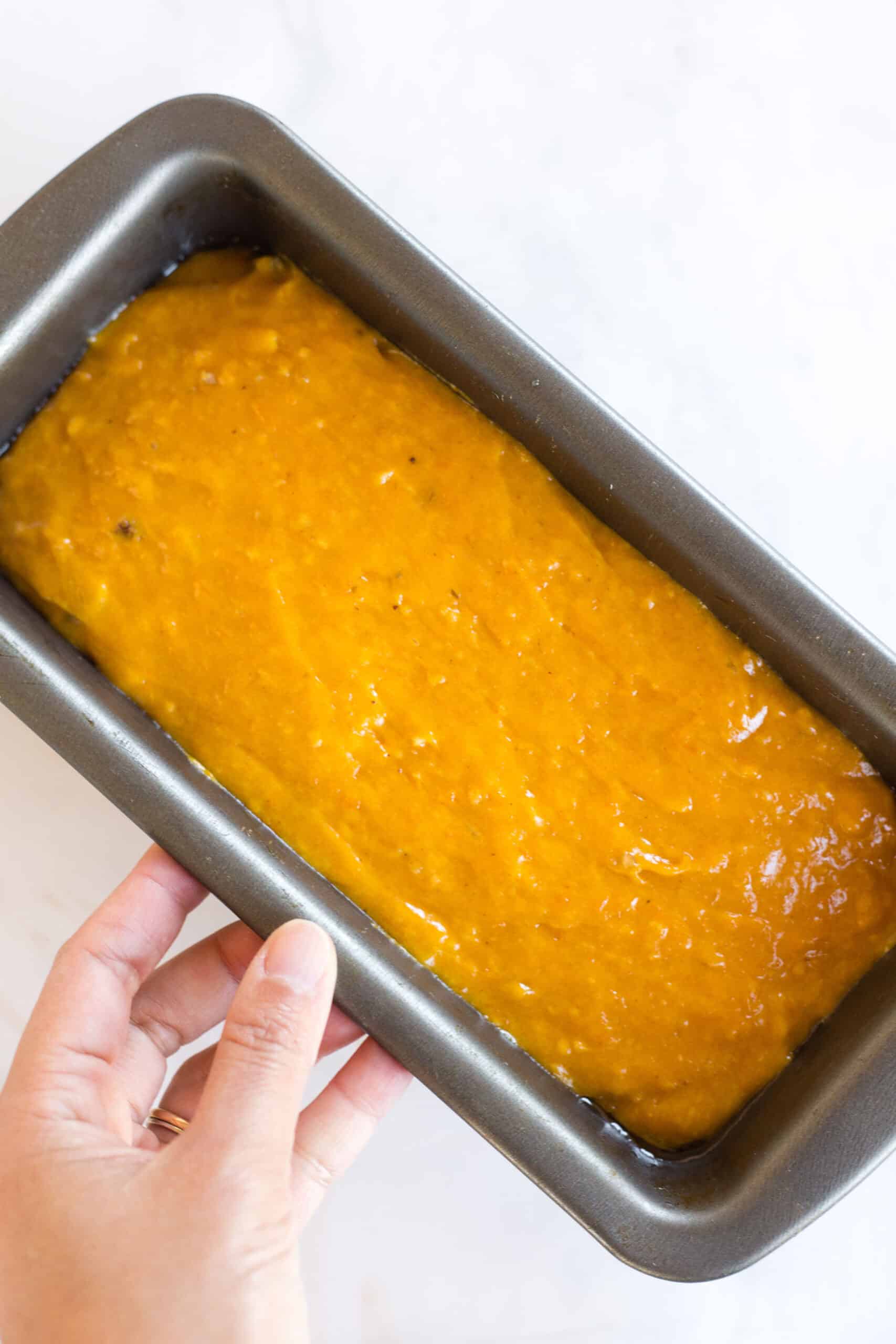 Holding a metal loaf pan with sweet potato bread batter.
