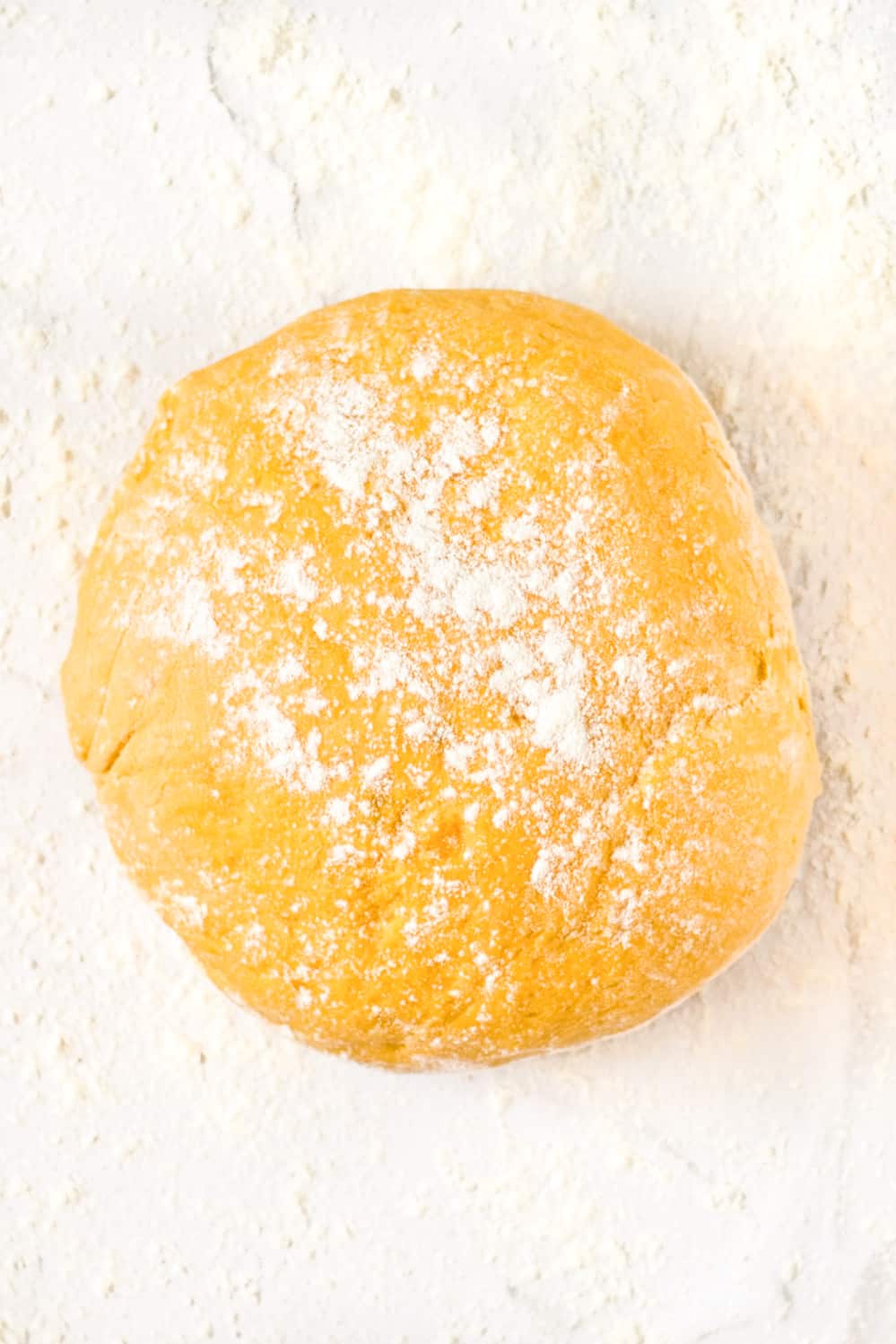Sweet potato gnocchi dough sprinkled with flour on a smooth surface.