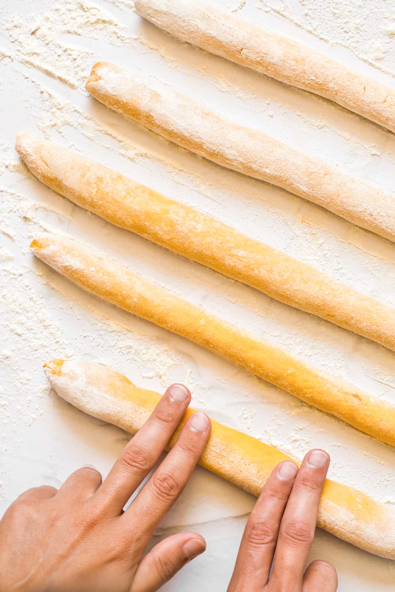 Rolling out gnocchi dough into long rolls.