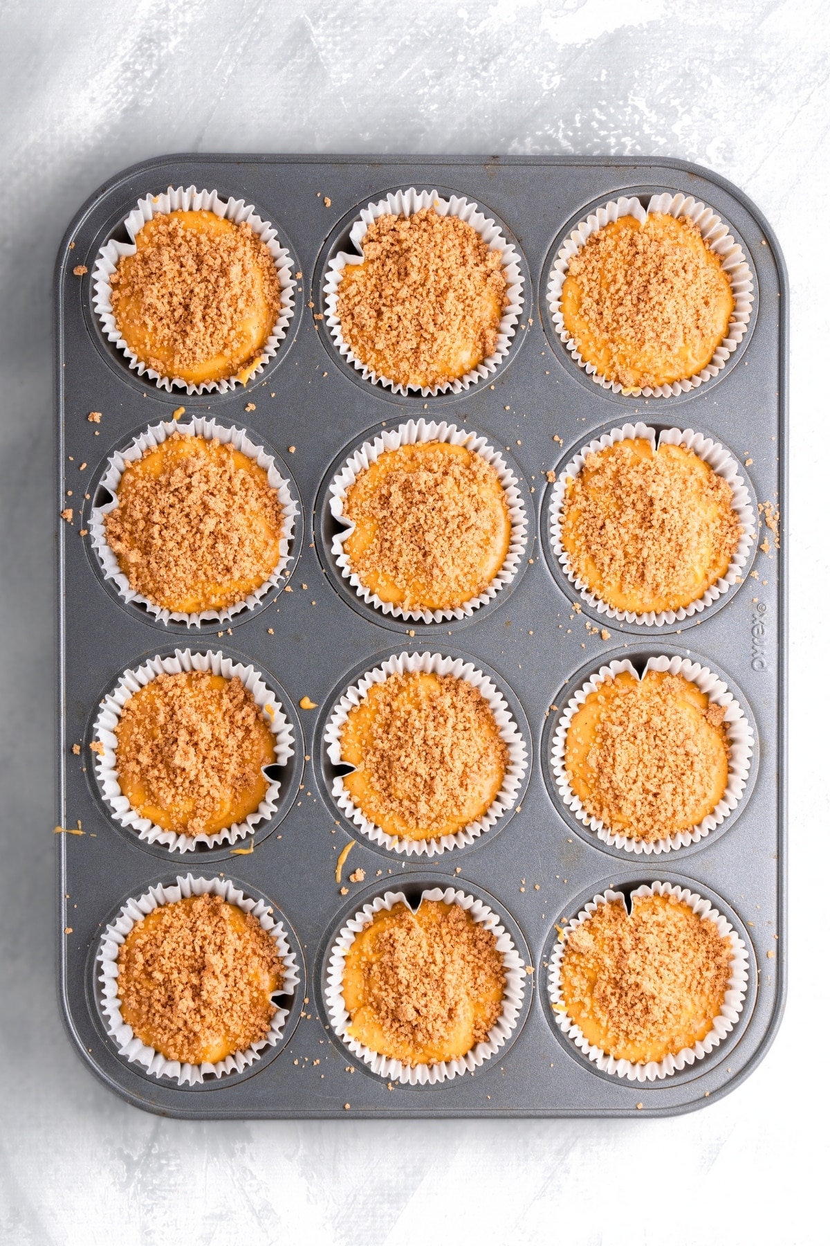 Muffin batter topped with streusel topping in muffin pan.