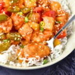 Spoon in a bowl of sweet and sour chicken and rice