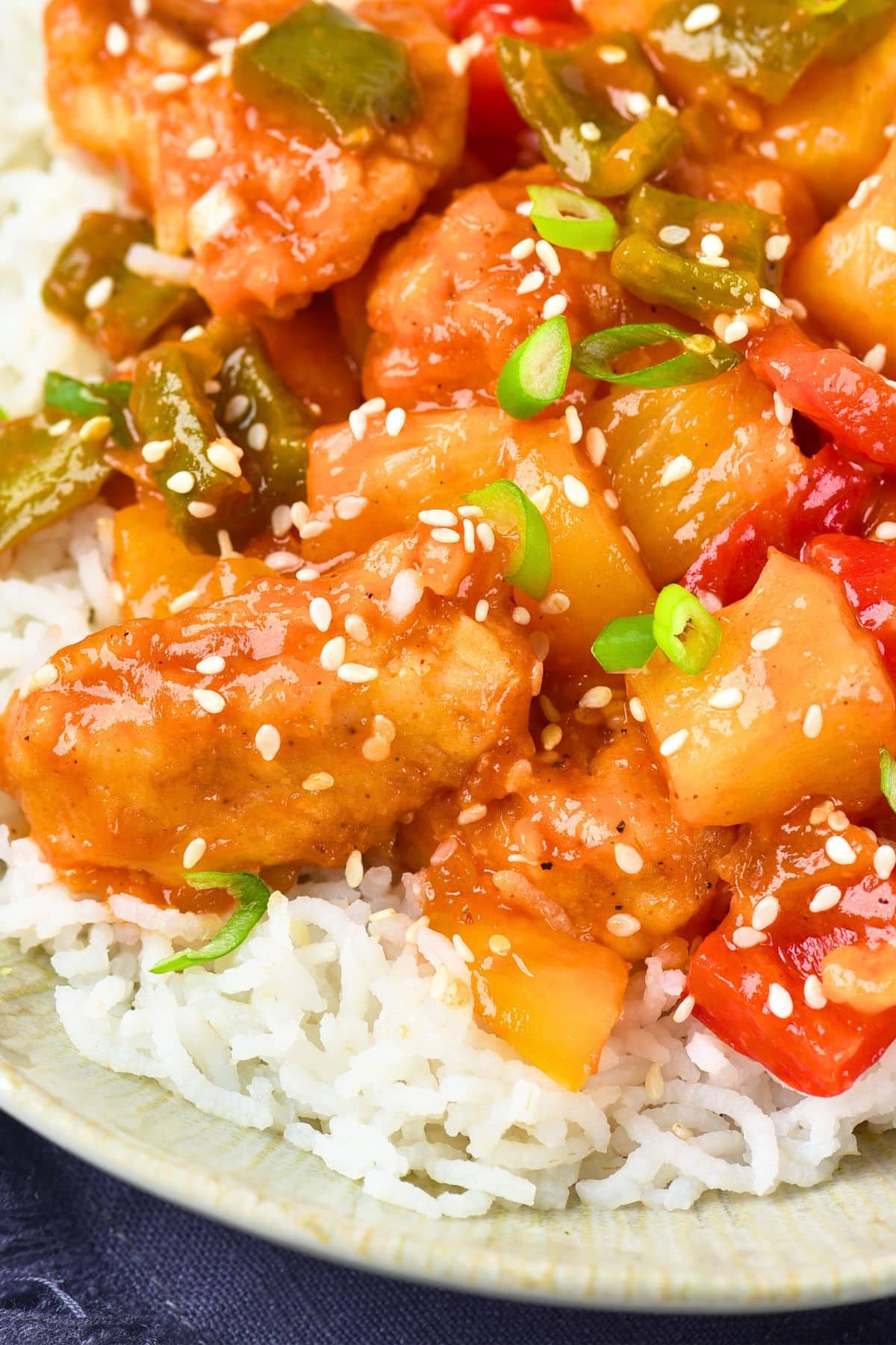 Up close view of gluten-free sweet and sour chicken sprinkled with sesame seeds and green onions.
