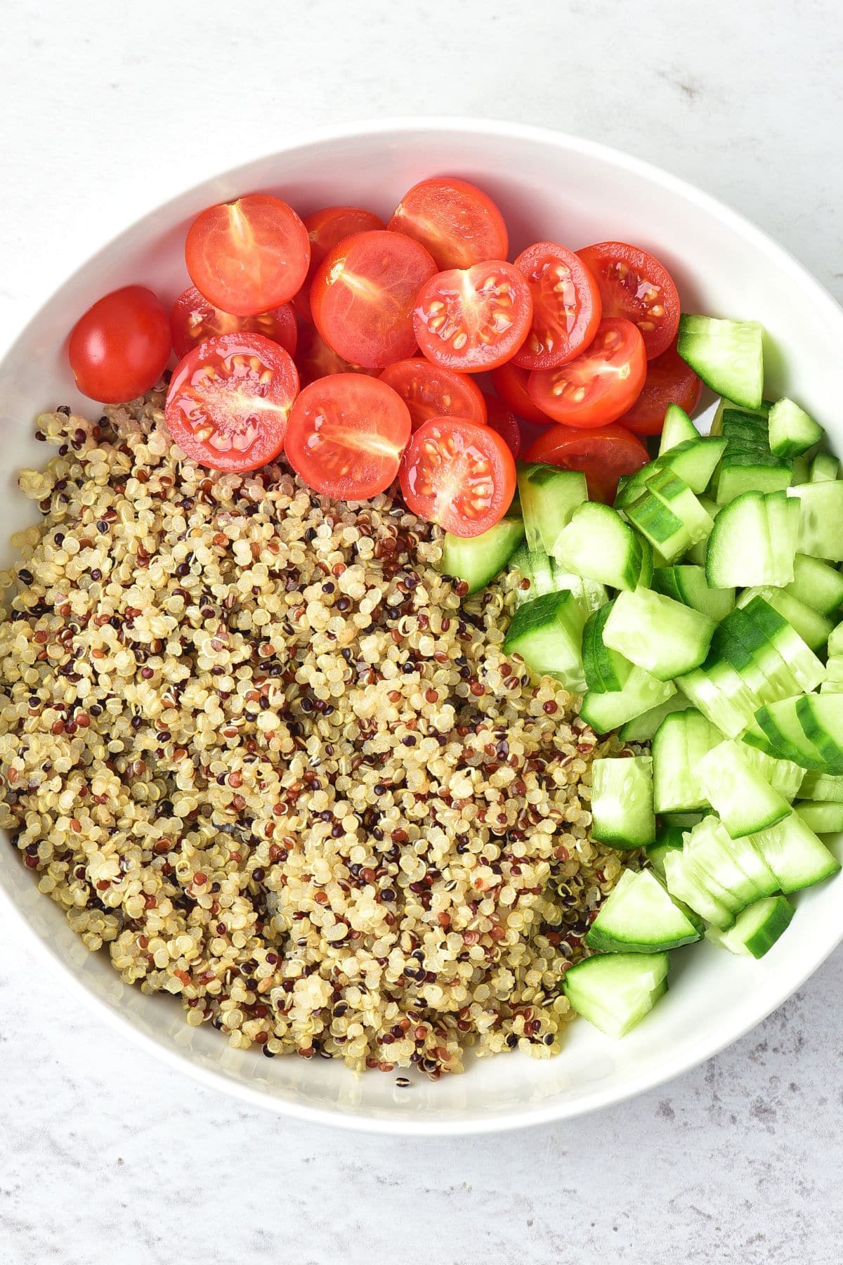 Grain-Free Tabbouleh A bowl of cooked quinoa with diced cucumbers and halved cherry tomatoes.