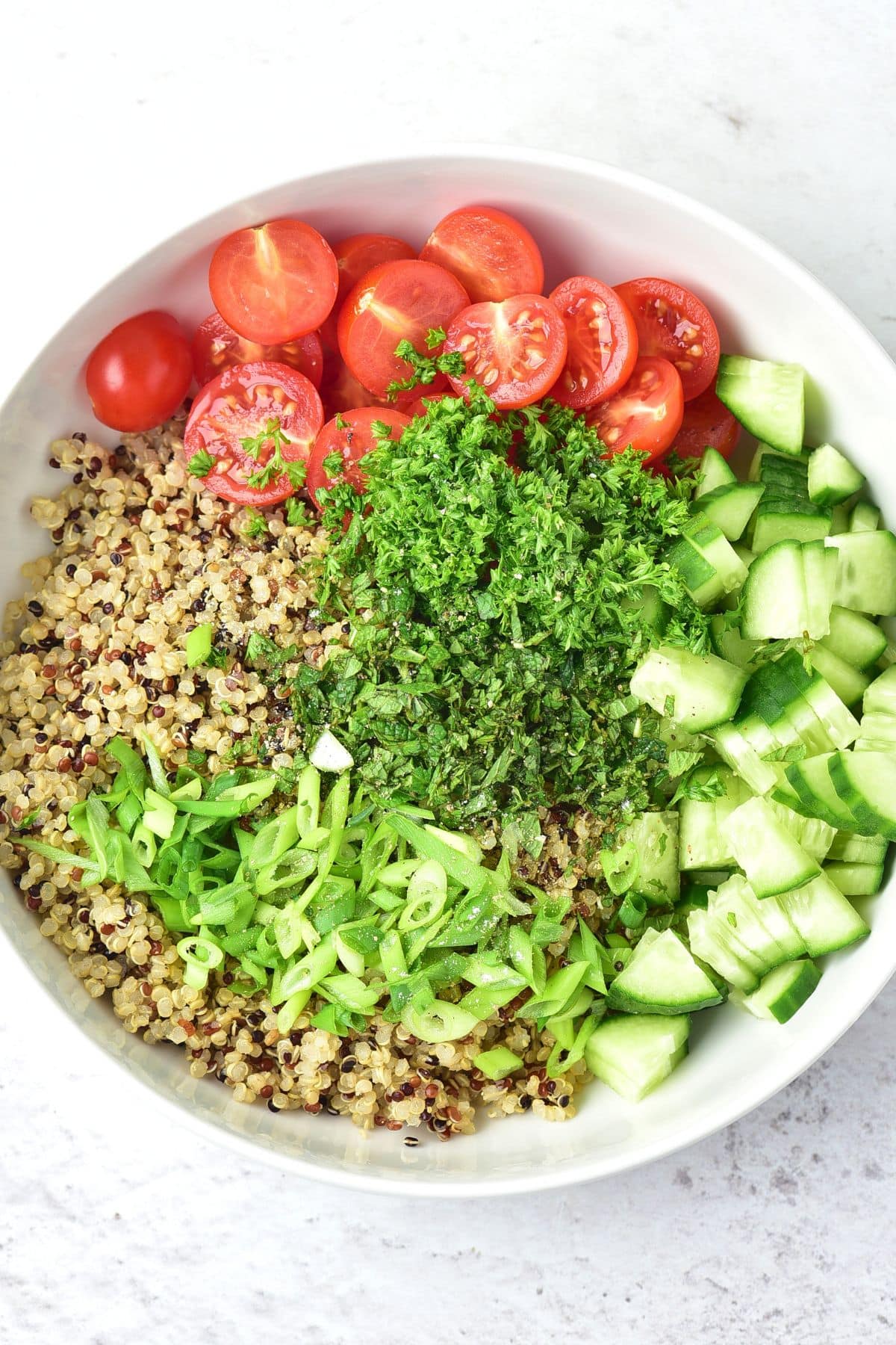 Gluten-Free Tabbouleh (Quinoa Tabbouleh Salad) A bowl of cooked quinoa, diced cucumber, halved cherry tomatoes and chopped parsley.