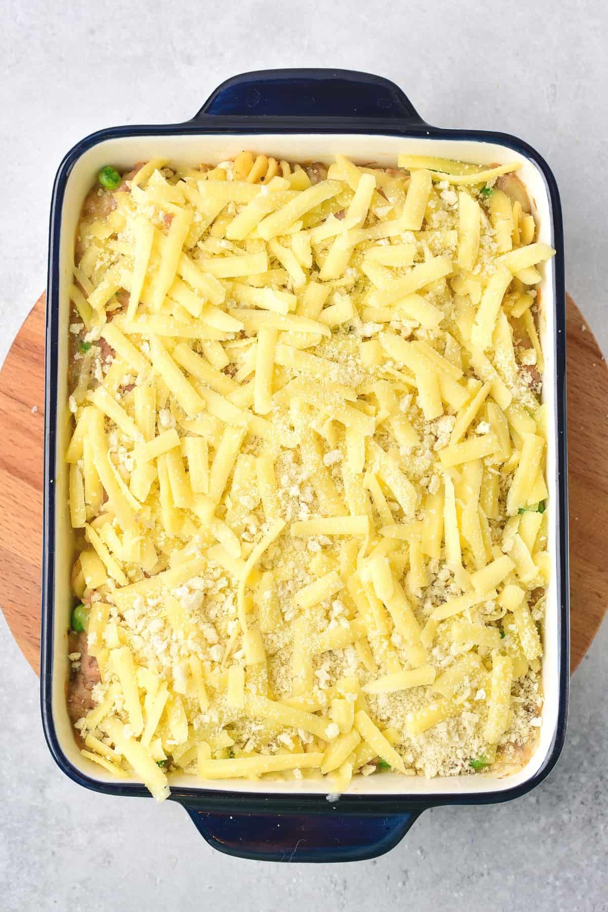 Tuna casserole topped with shredded cheese in baking dish.