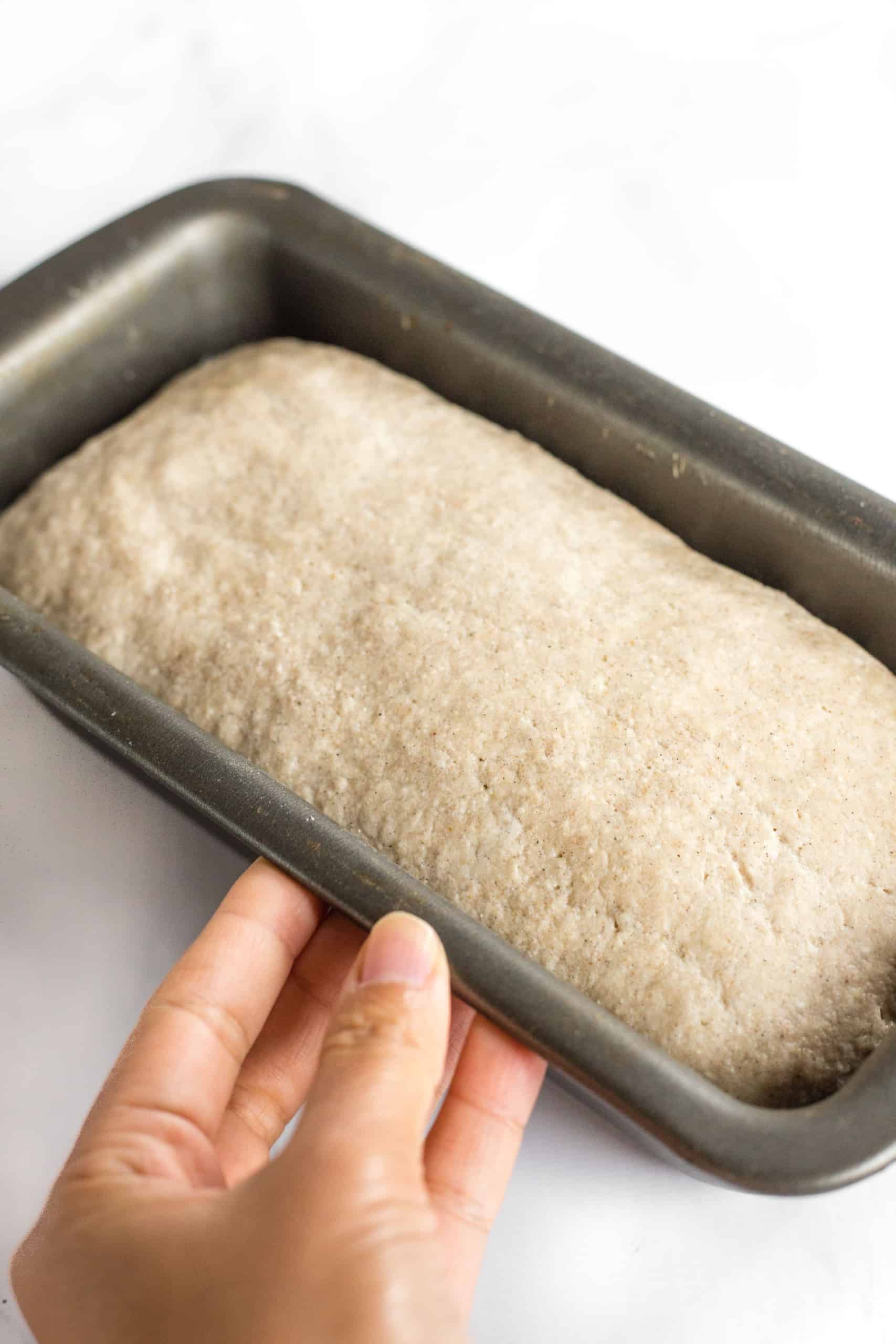 Holding a metal loaf pan with risen bread dough.