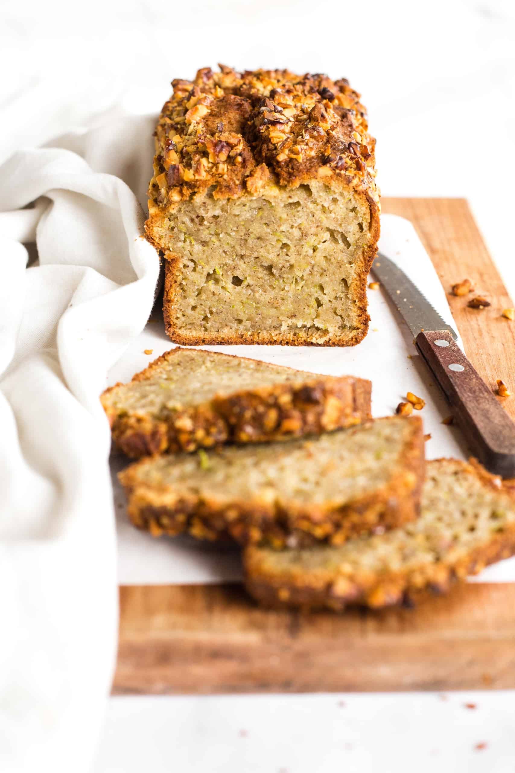 Half-sliced loaf of gluten-free zucchini bread on a parchment-lined wooden board.