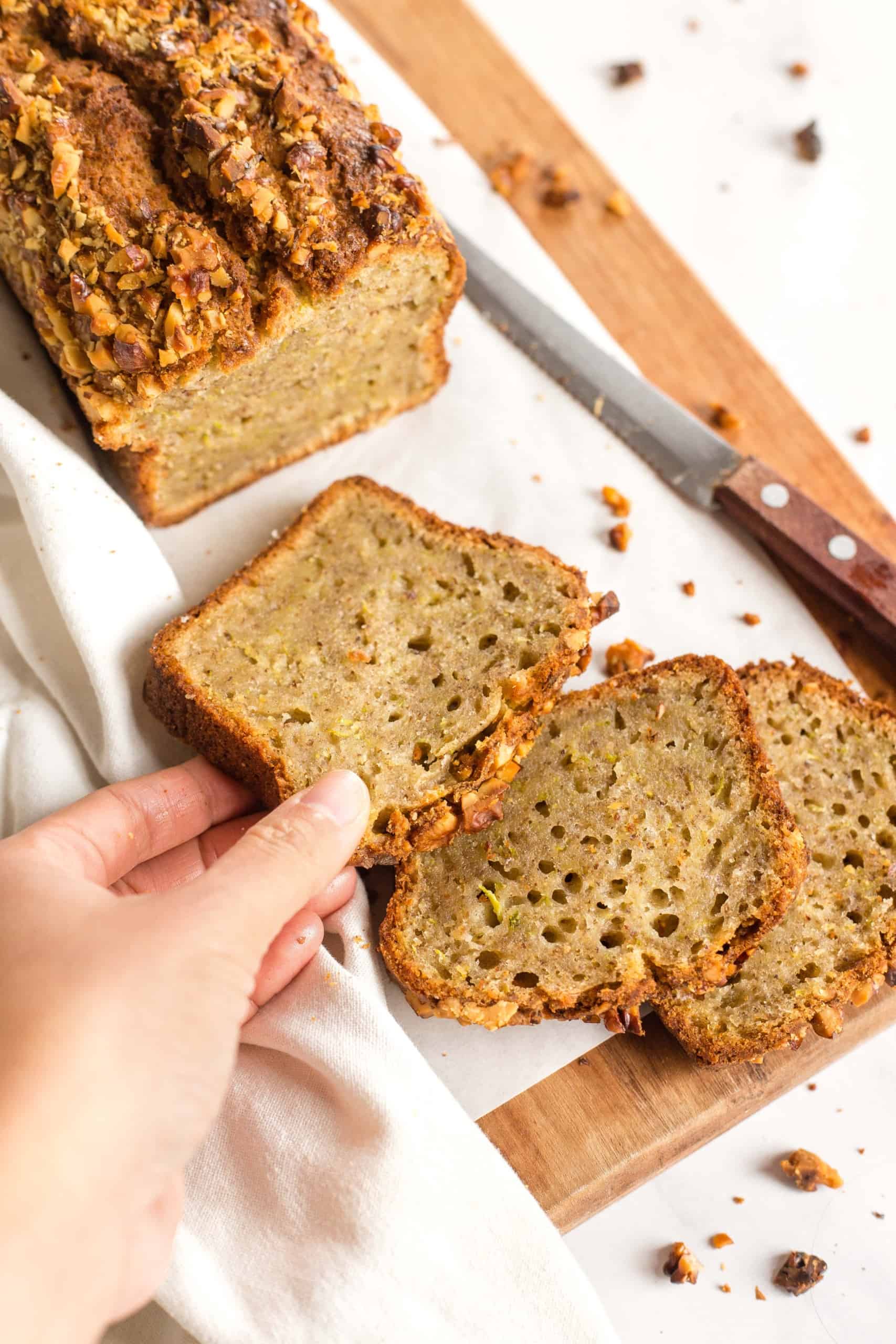 Reaching for a slice of zucchini bread from a parchment-lined board.