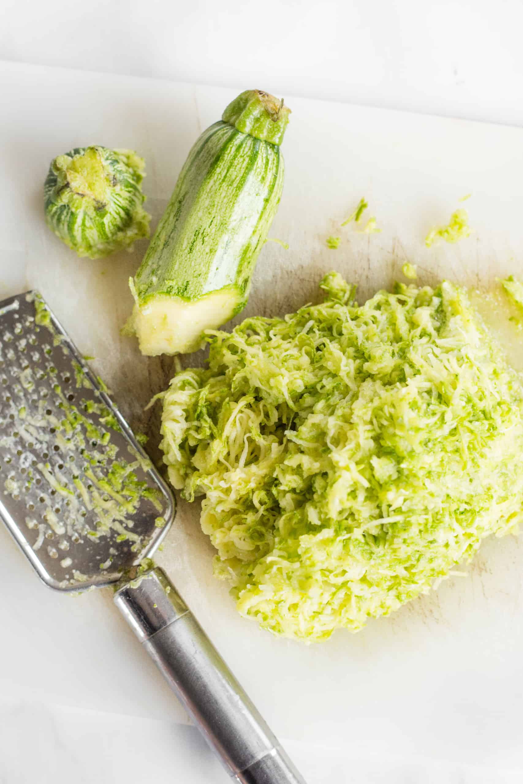 Grated zucchini and a cheese grater on a chopping board.