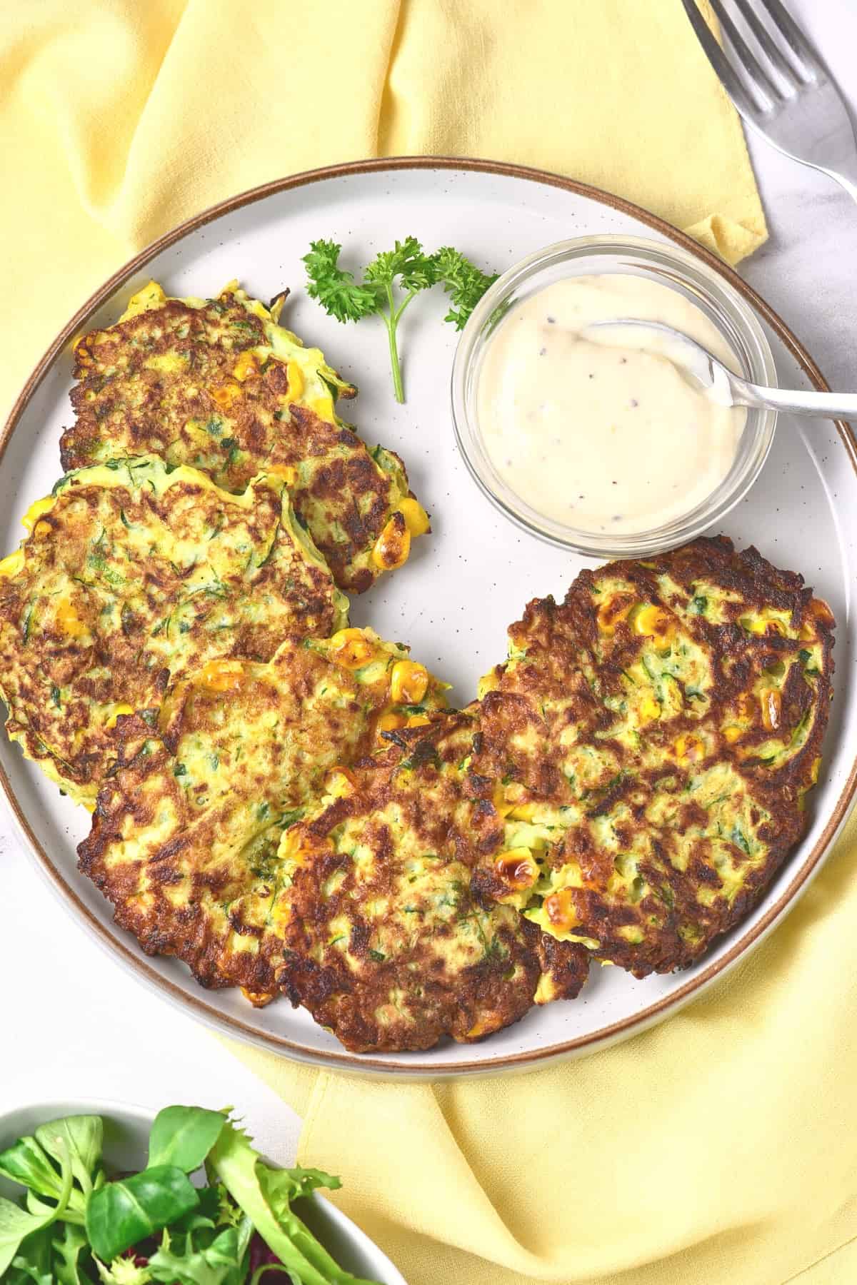 Top down view of zucchini fritters and garlic aioli on a plate.