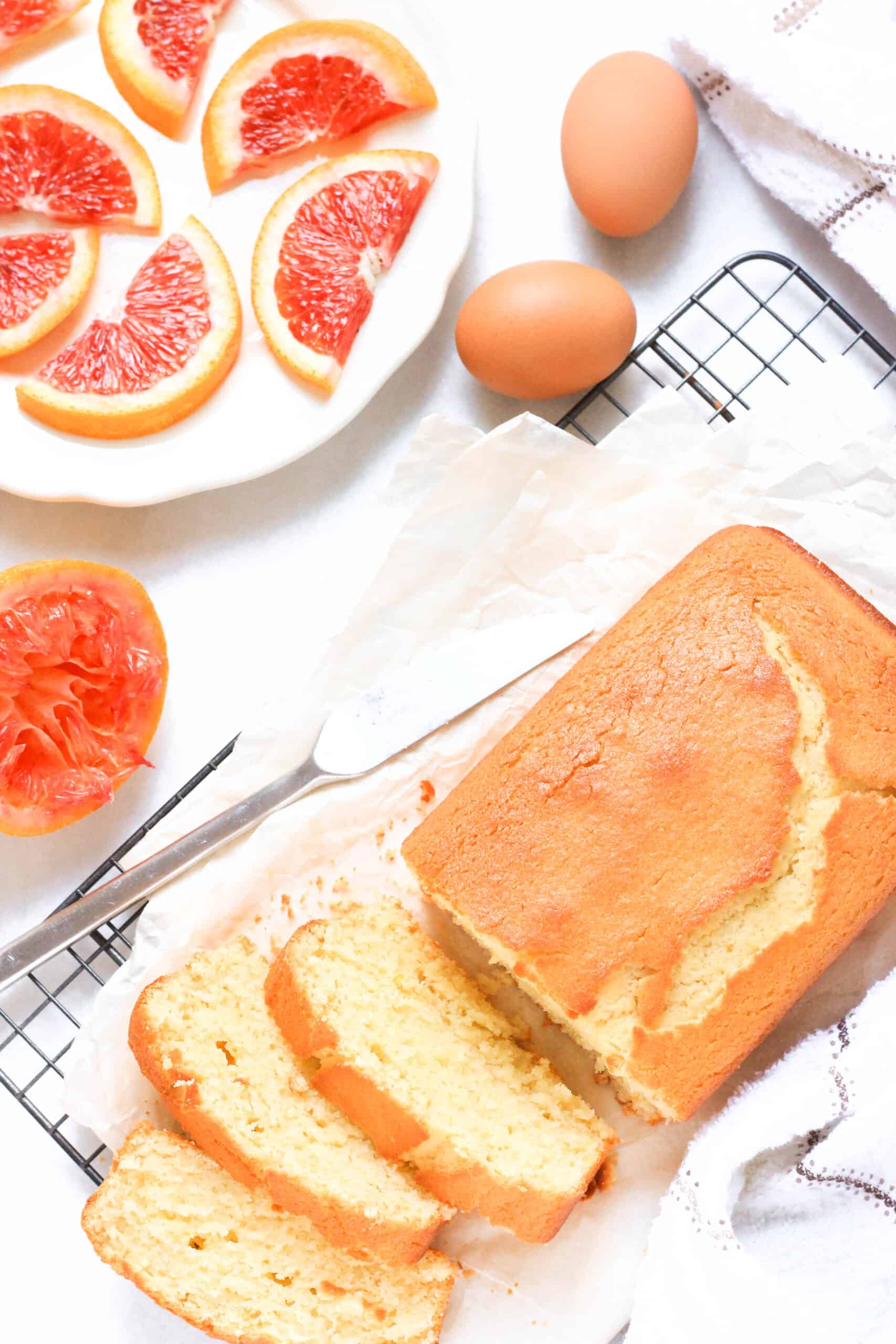 Top down view of blood orange pound cake on wire rack and slices of blood oranges.