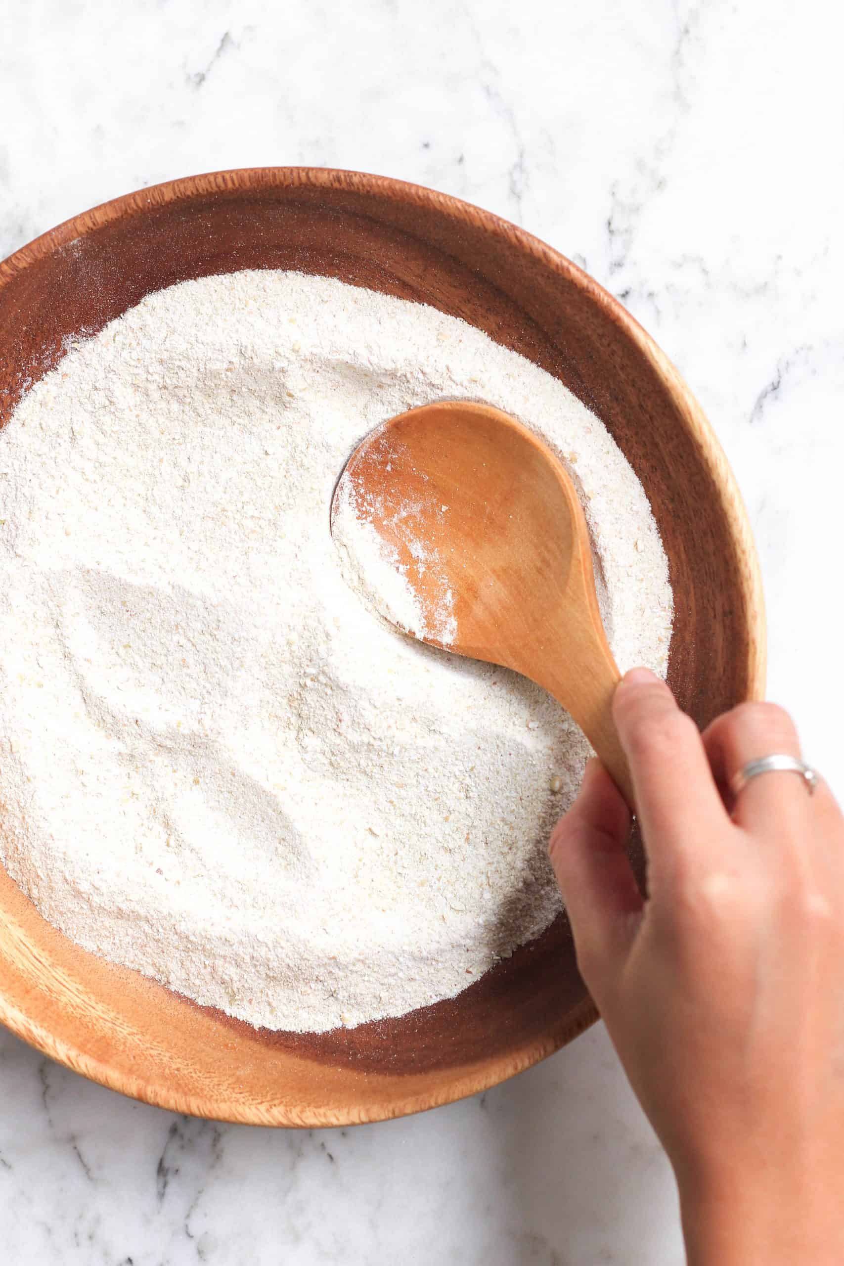 Holding a wooden spoon over a bowl of buckwheat flour.