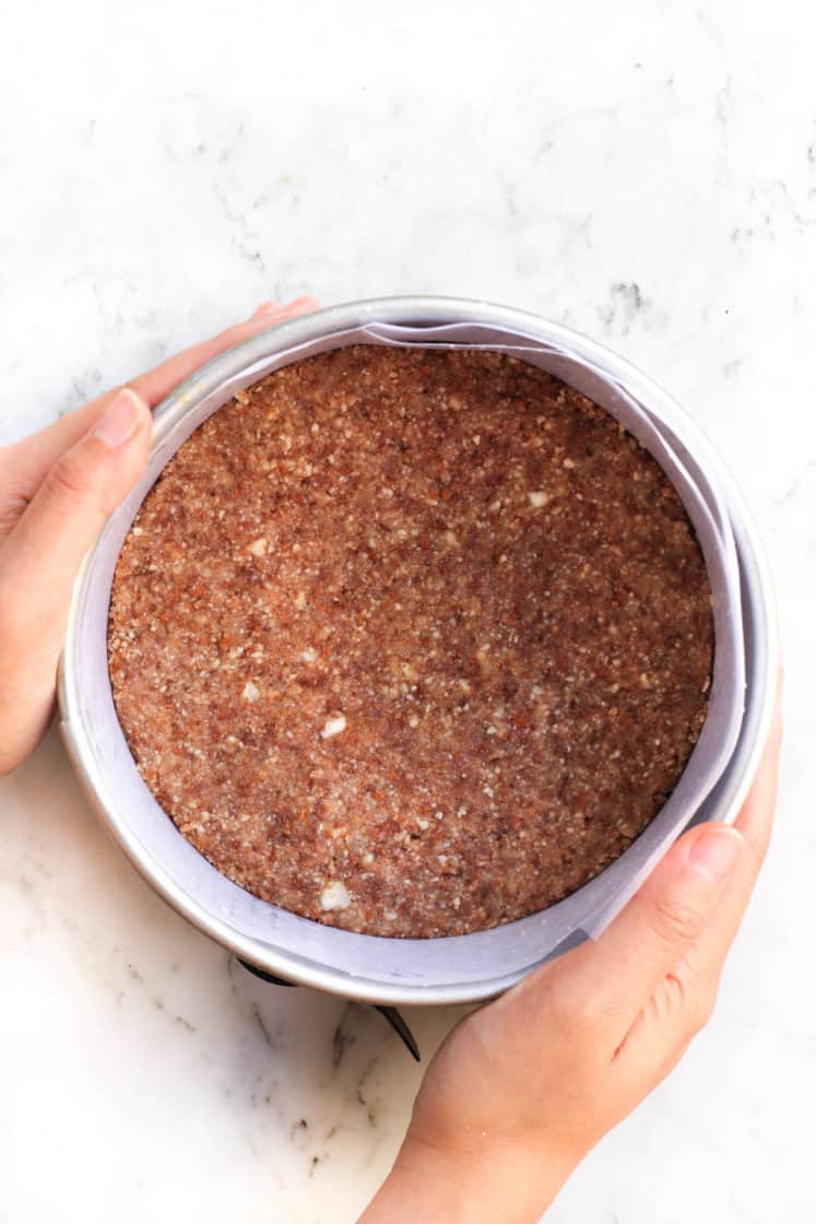 Hands holding a parchment-lined springform pan with crust.