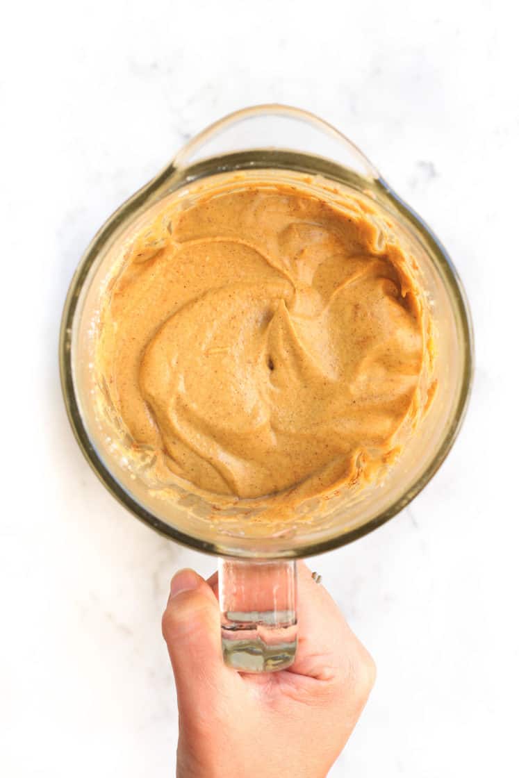 Hand holding a blender with creamy processed vegan pumpkin cheesecake filling.
