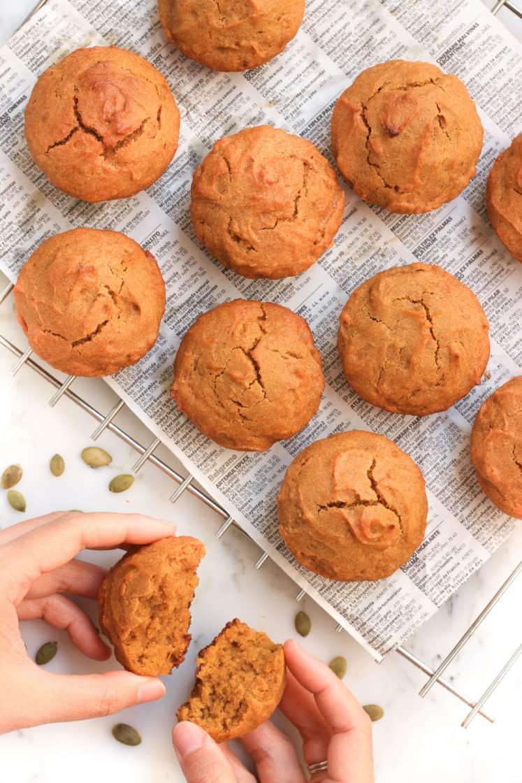 Gluten-free pumpkin muffins on a cooling rack and hands dividing a muffin into half.