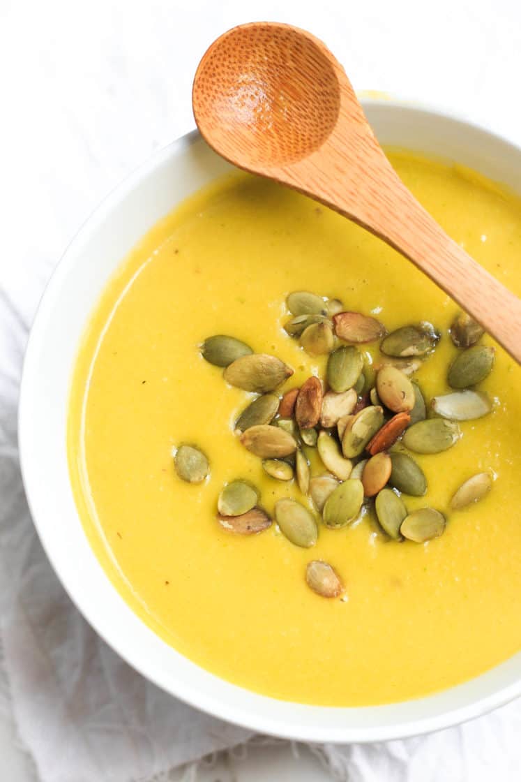 Pumpkin soup with pumpkin seeds in a bowl with a wooden spoon.