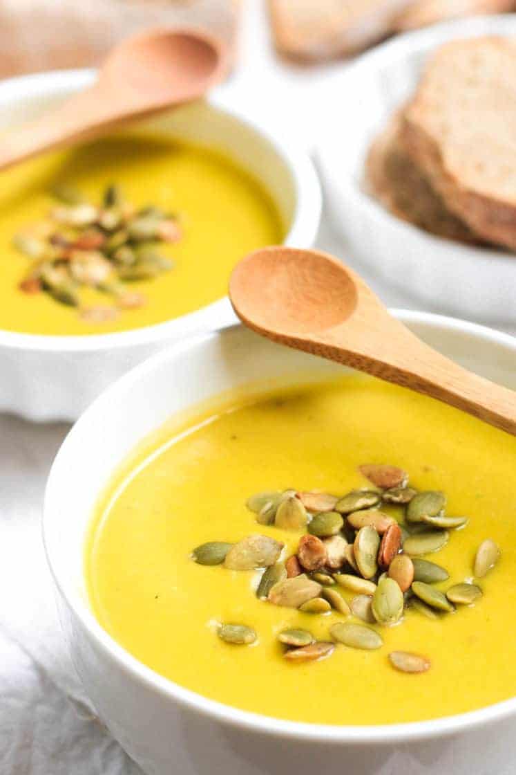 A close up shot of vegan pumpkin soup sprinkled with pumpkin seeds in a white bowl.