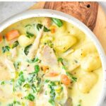 Top down view of a bowl of chicken and gnocchi soup on wooden board.
