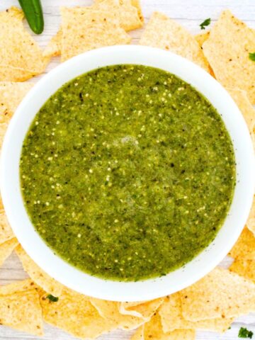 Top down view of a bowl of tomatillo sauce surrounded by nachos.