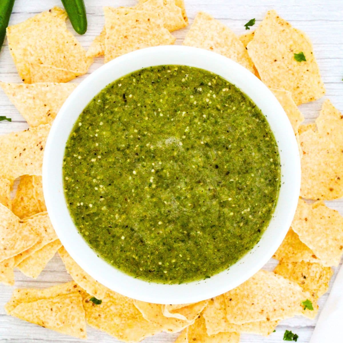 Top down view of a bowl of tomatillo sauce surrounded by nachos.