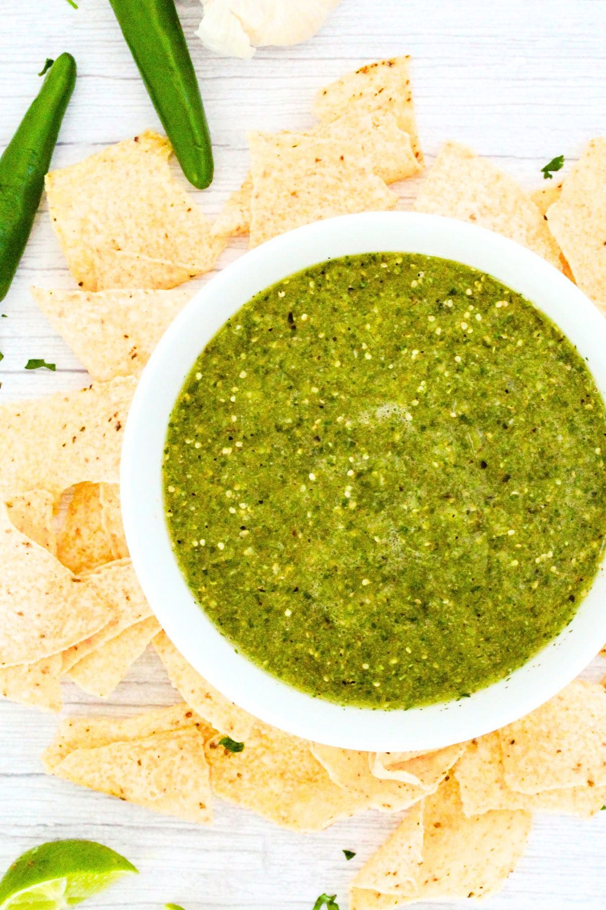 A bowl of green tomatillo sauce surrounded by corn tortilla chips