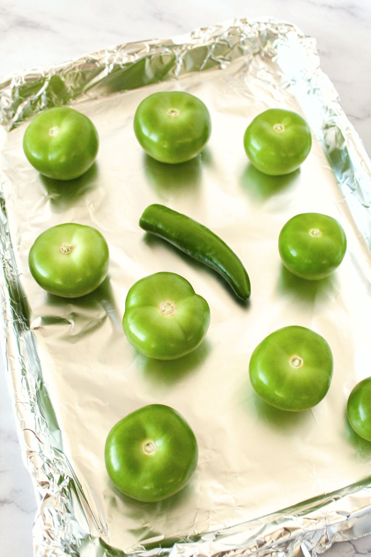 Raw green tomatillos on aluminum foil-lined baking sheet