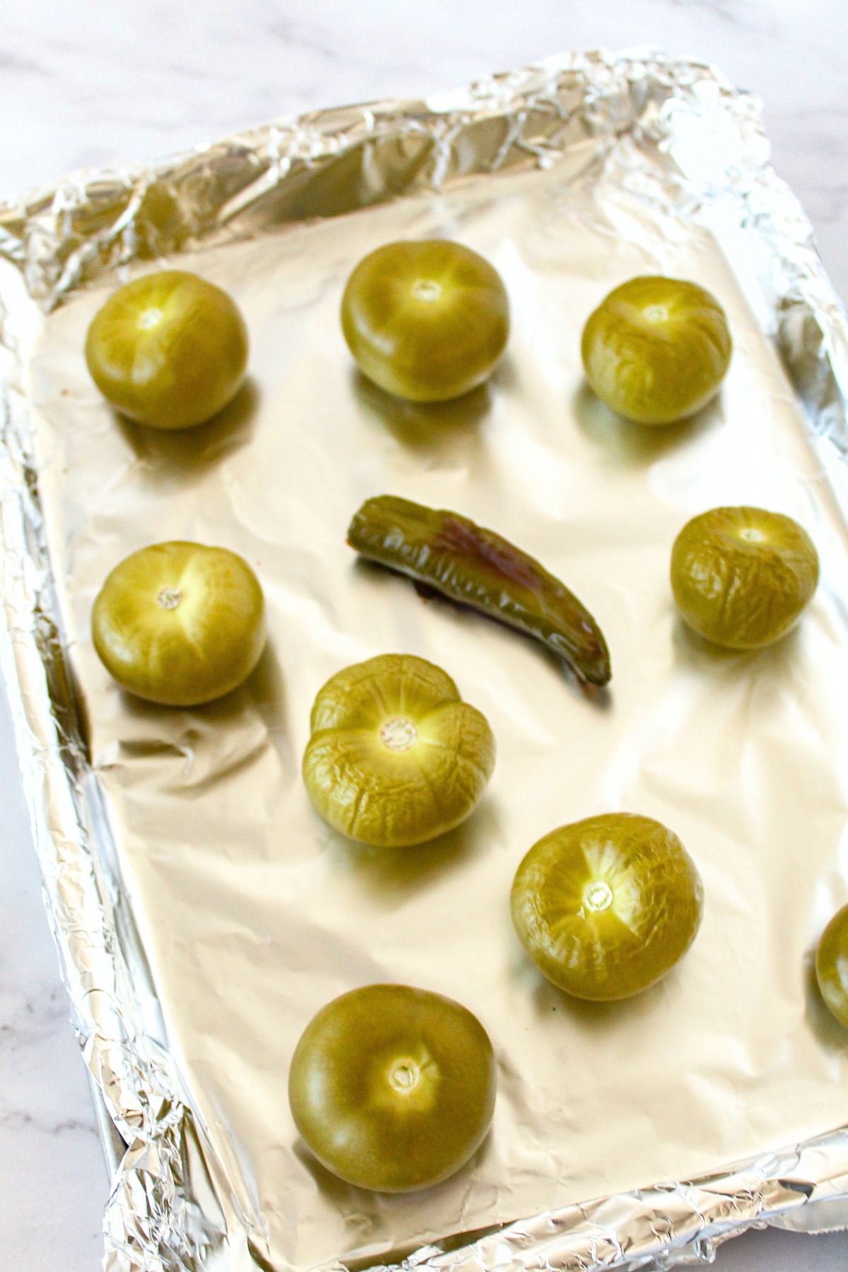 Roasted green tomatillos and serrano pepper on baking sheet