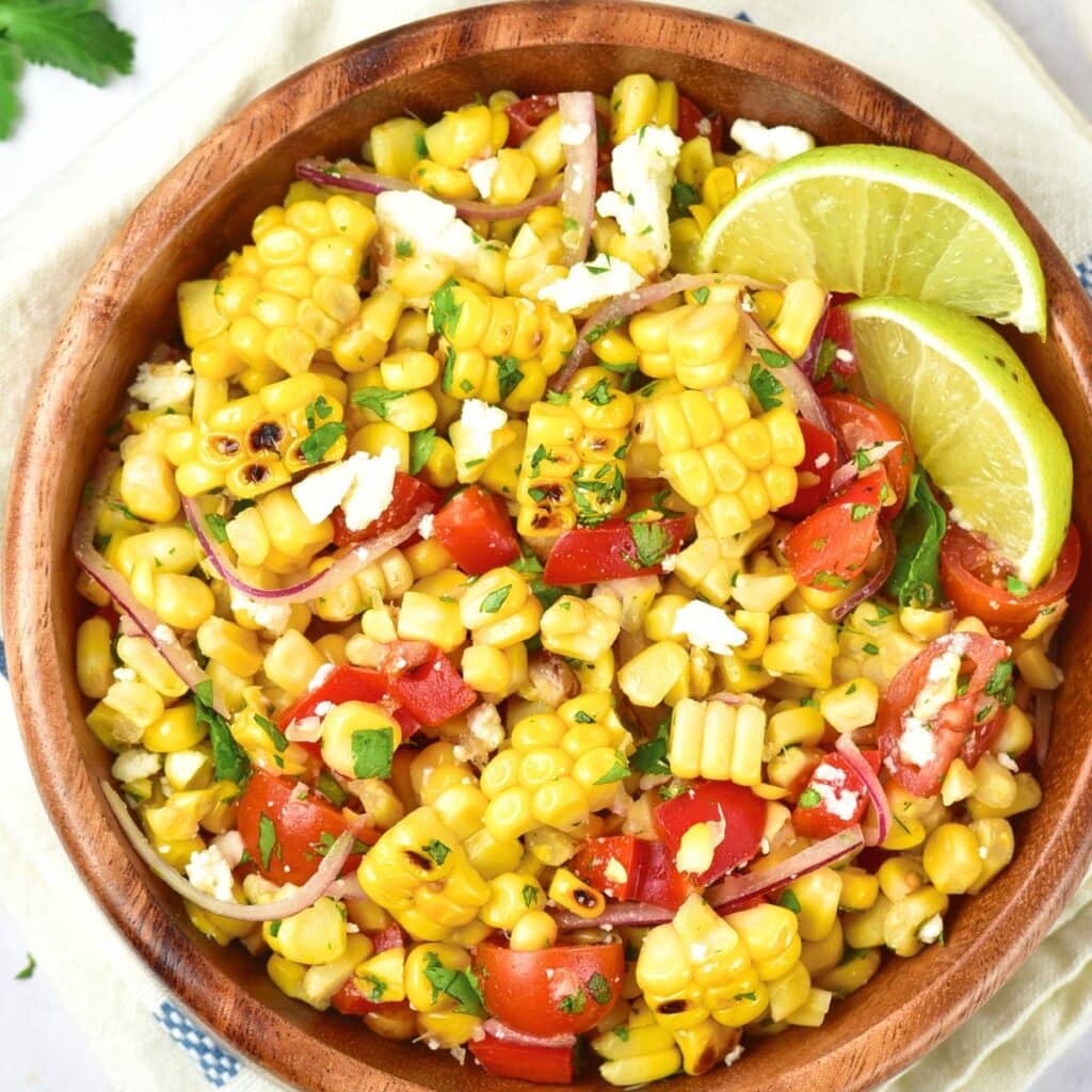 Top down view of a bowl of grilled corn salad with lime wedges.