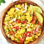 Top down view of a bowl of grilled corn salad with lime wedges.
