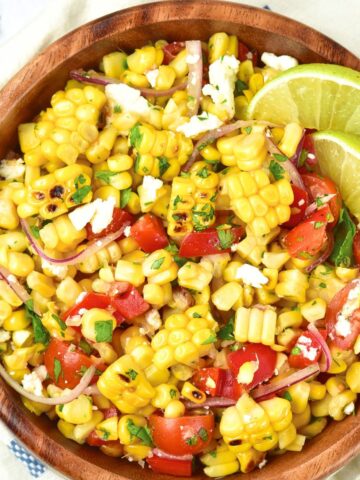 Top down view of a bowl of grilled corn salad with lime wedges.