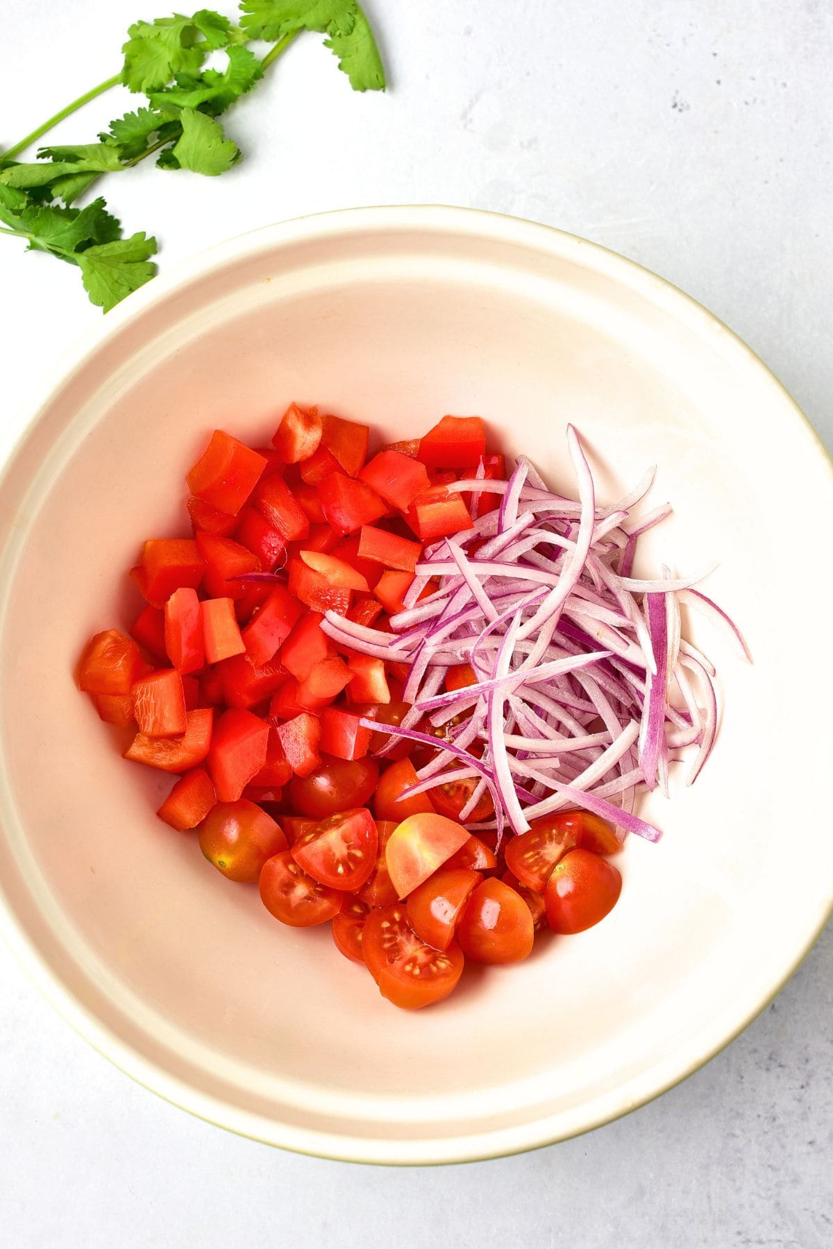 How to Make Grilled Corn Salad Top down view of diced tomatoes and sliced red onions in white bowl.