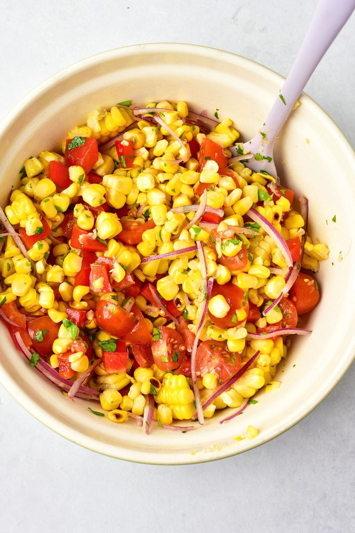 Grilled corn kernels, sliced onions, diced tomatoes in a white bowl.