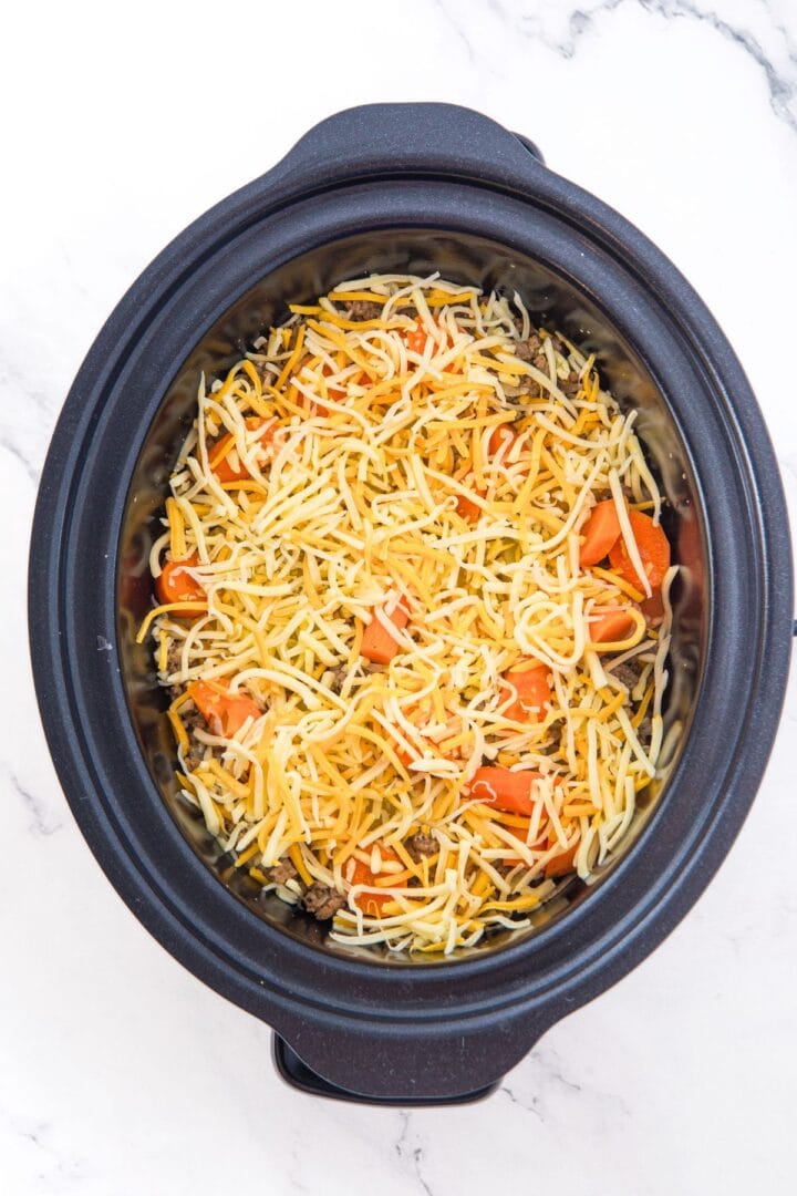 A slow cooker with ground beef topped with shredded cheese.