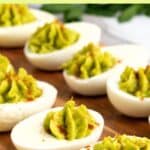 Guacamole deviled eggs on wooden board.