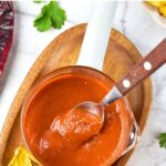 Top down view of jar of homemade guajillo sauce on wooden board.