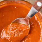 Scooping a spoonful of guajillo sauce from a jar.